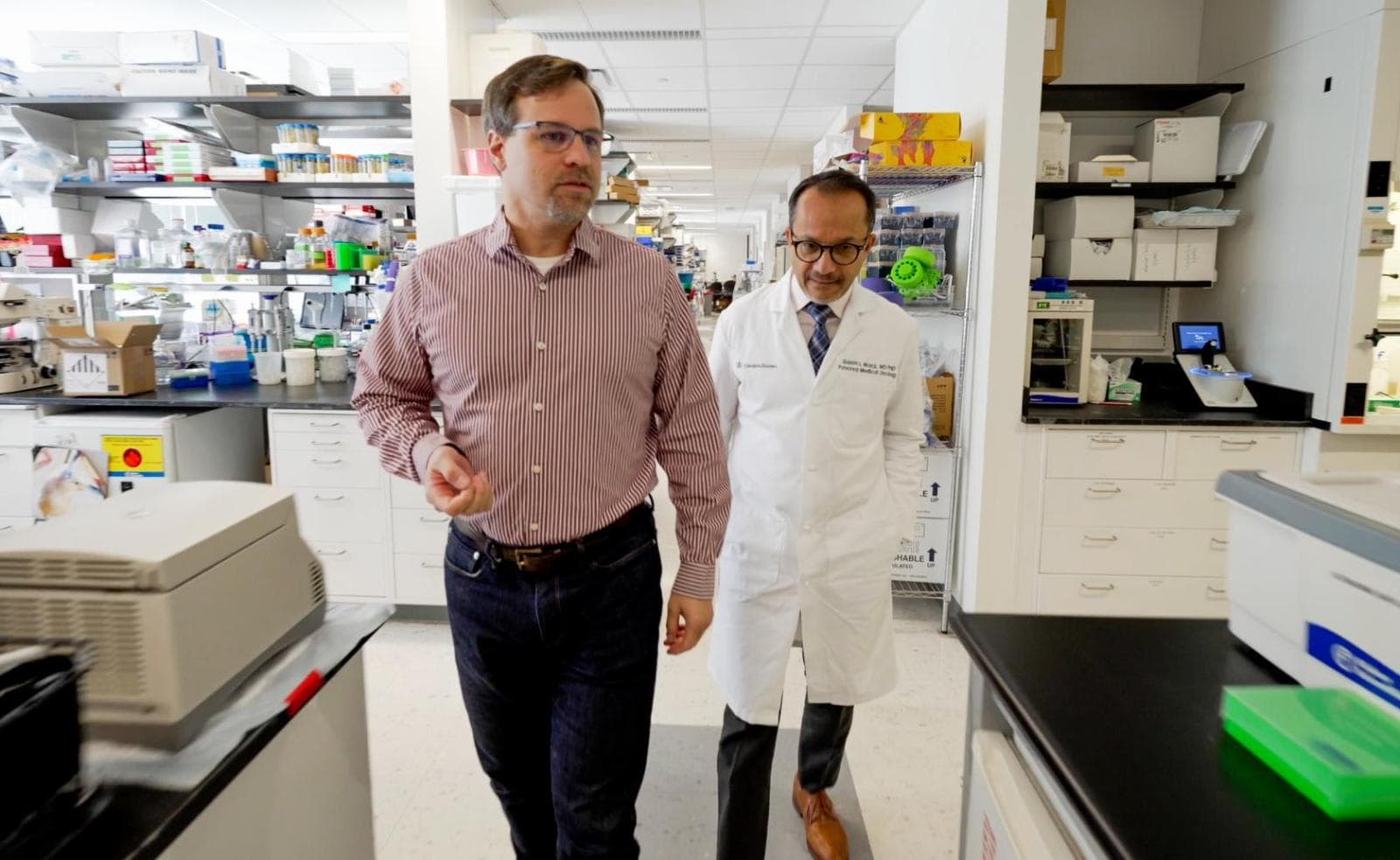 Two men in lab coats walking through a lab